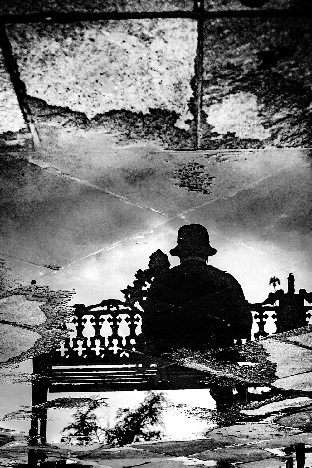Reflection of a man sitting on a bench in a puddle, black and white photograph